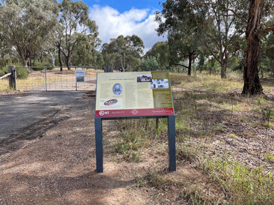 A walking group gathered around the Lyneham walk trail sign. They are watching a tour guide presenting.