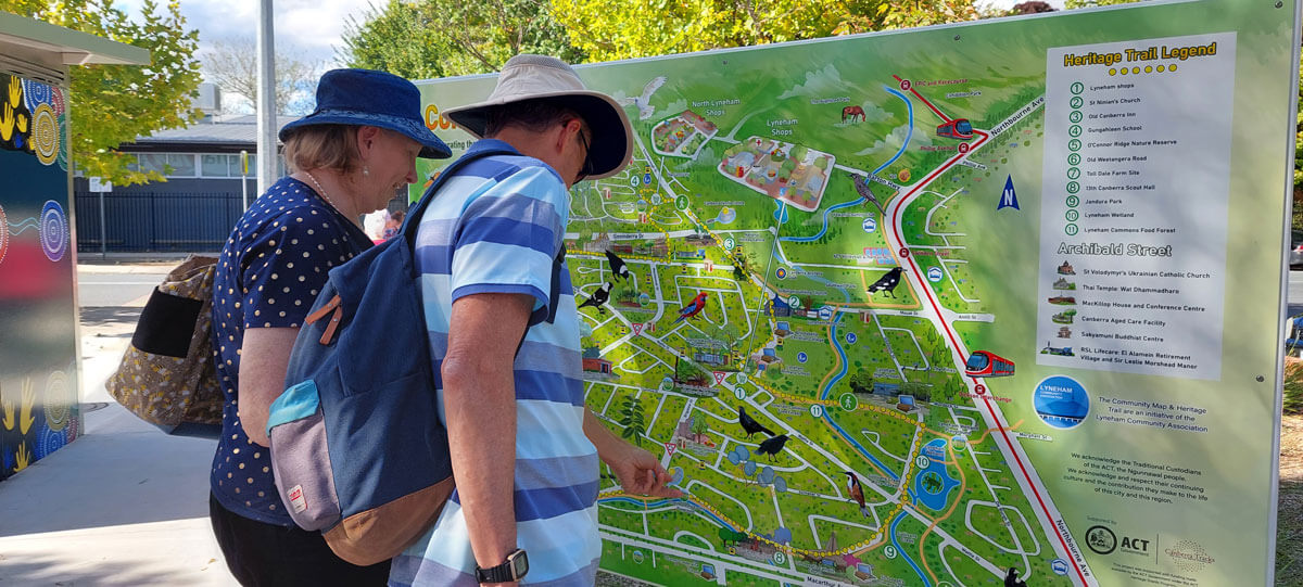 A man and woman looking at the large Heritage Trail sign located at the Lyneham shops on Wattle street.